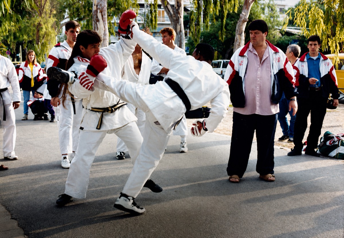 Scott Batey competing in kumite in white gi and red headgear, representing the USA at the Mediterranean Games in Greece.