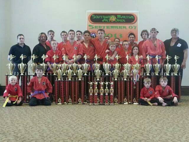 The team in red gis behind a wall of tournament trophies at the 2013 Southwest Martial Arts Open.
